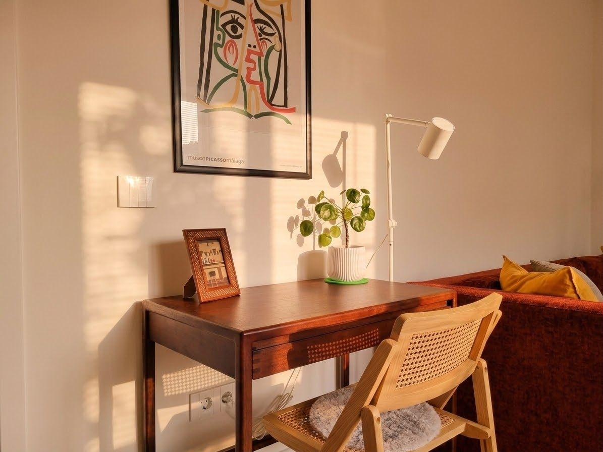 Vintage writing desk with a cane chair, framed print above, beside a velvet sofa in rust